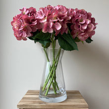 Load image into Gallery viewer, Field &amp; Rose pink artificial silk hydrangea stem, 53cm, in a clear glass vase on a wooden table.

